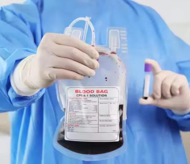 A technician in protective clothing handling a unit of whole blood and a crossmatch sample